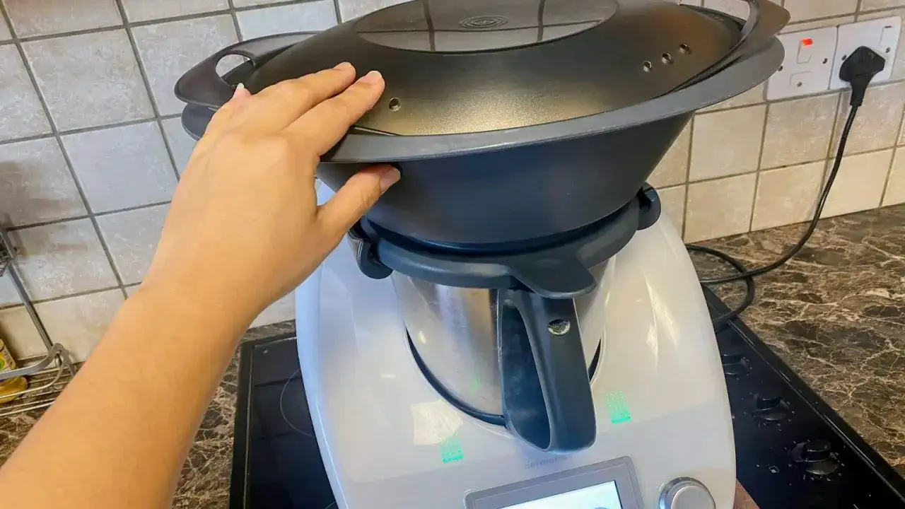 Dłoń zamyka pokrywę Thermomixa, przygotowując go do transportu. Wtyczka jest podłączona do gniazdka.