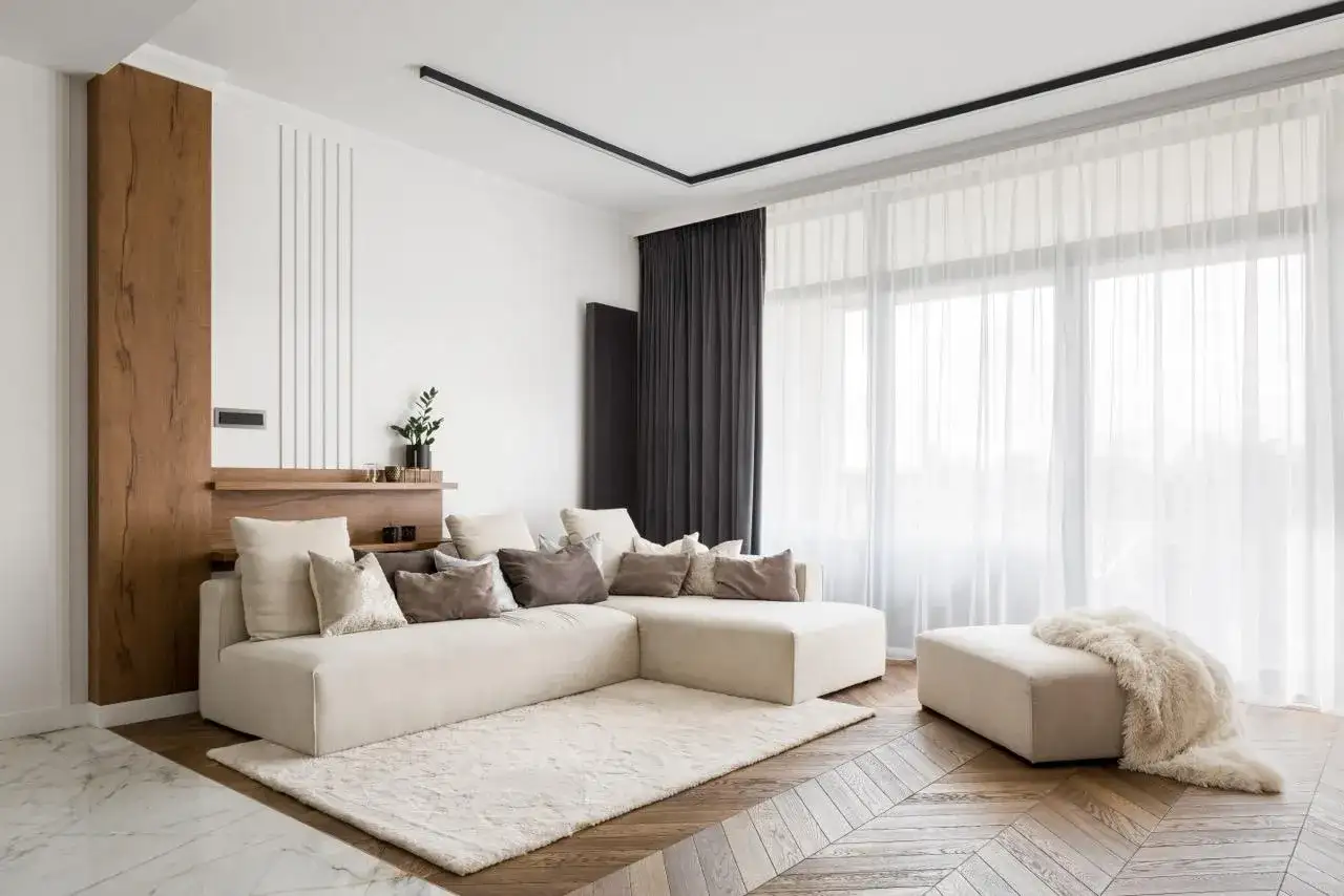 Nowoczesny salon z beżową sofą i puszystym dywanem. Elegancki karnisz do zabudowy dyskretnie podkreśla zasłony.