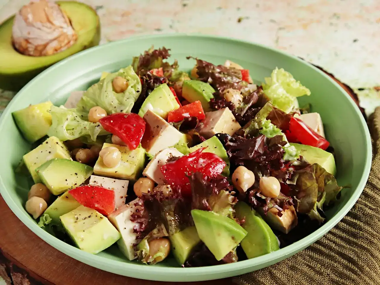 Frischer veganer Salat mit Avocado, Kichererbsen, Tofu und roten Paprikastücken in einer hellgrünen Schüssel.