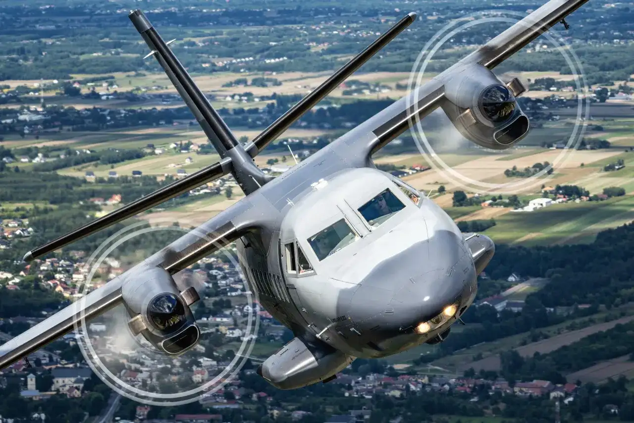 Samolot transportowy w locie, z widocznymi wirującymi śmigłami, nad polami i lasami. Widok z lotu ptaka, jakbyśmy byli na pokazach lotniczych kiedy air show w Radomiu.