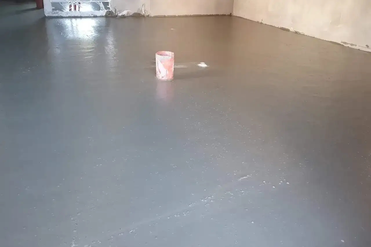 Świeżo wylany, gładki **pianobeton** na podłodze. W tle widać wiaderko i instalacje.