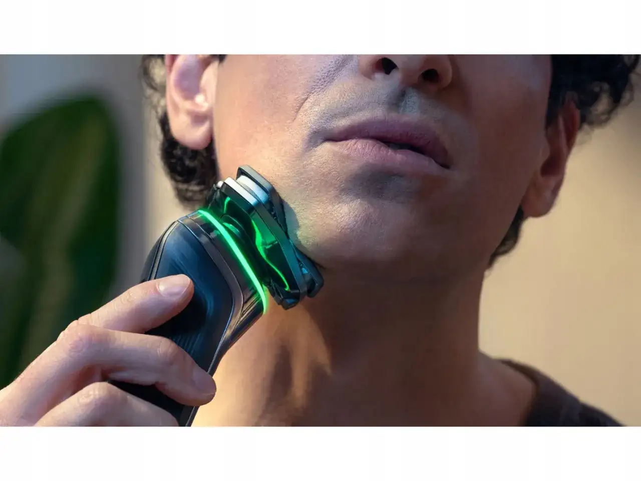 Mężczyzna goli twarz golarką Philips z zielonym podświetleniem.
