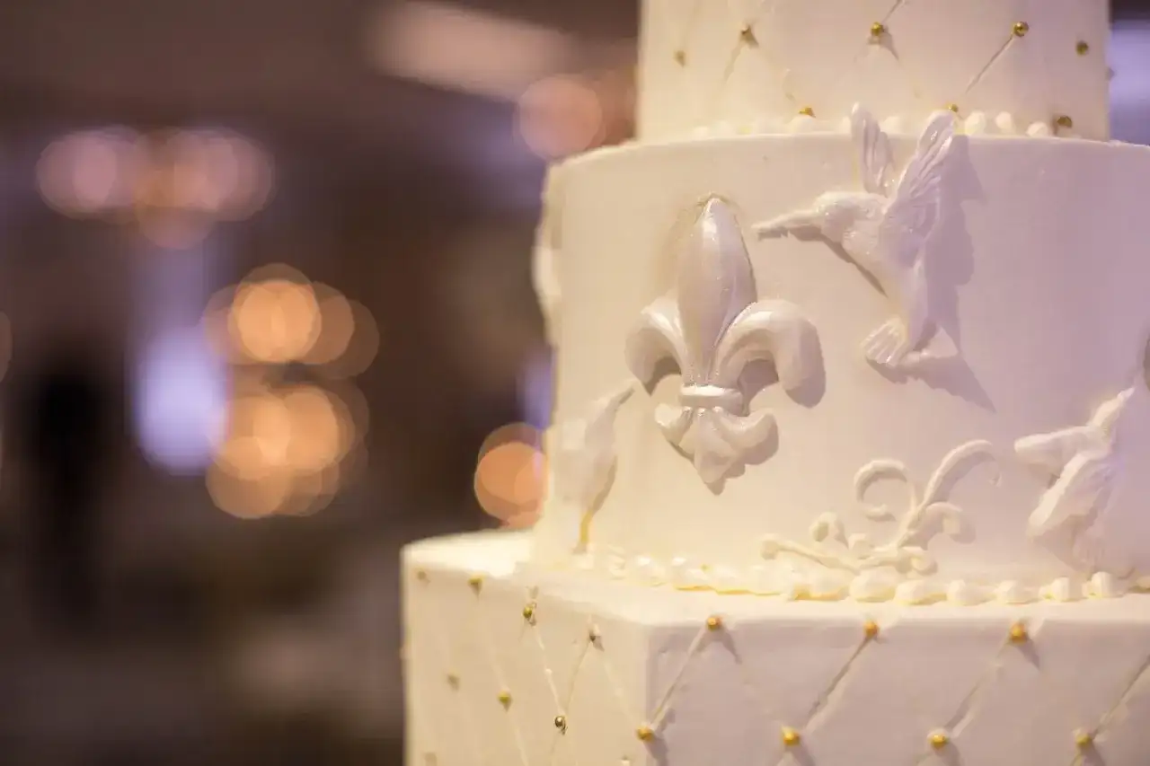 Elegancki tort weselny z ozdobami z masy cukrowej, jak przykleić ozdoby z masy cukrowej do tortu? Delikatne lilie i ptaszki zdobią białe warstwy.
