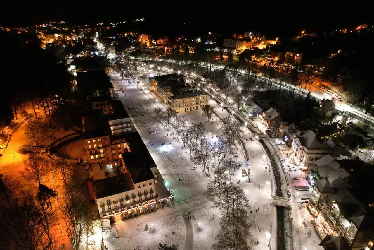 Zimowy wieczór w Krynicy-Zdroju. Oświetlone budynki i deptak przyciągają spacerowiczów, tworząc magiczną atmosferę. Krynica-Zdrój atrakcje wieczorem w śnieżnej odsłonie.
