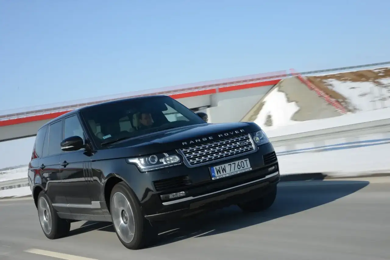 Czarny Range Rover Vogue pędzi po drodze, za nim śnieżne krajobrazy i błękitne niebo.