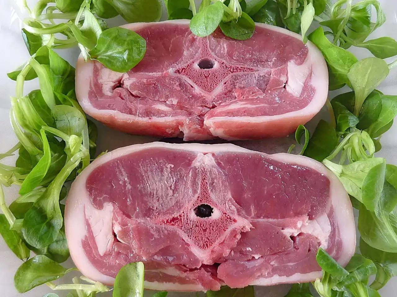 Dwa soczyste kotlety jagnięce otoczone świeżą sałatą. Zastanawiasz się, ile kosztuje kilogram jagnięciny?