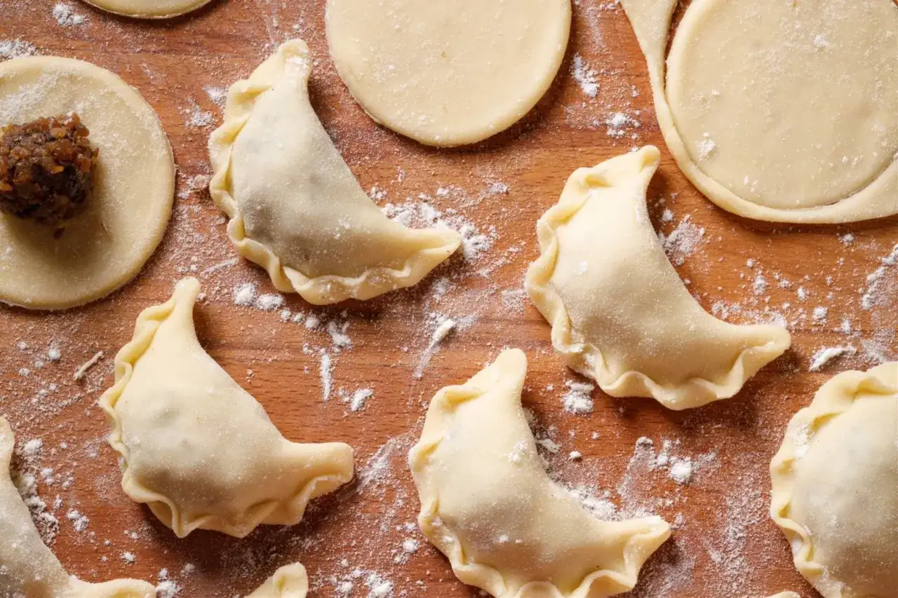 Surowe pierogi z kaszą gryczaną i twarogiem na drewnianej desce, posypane mąką.
