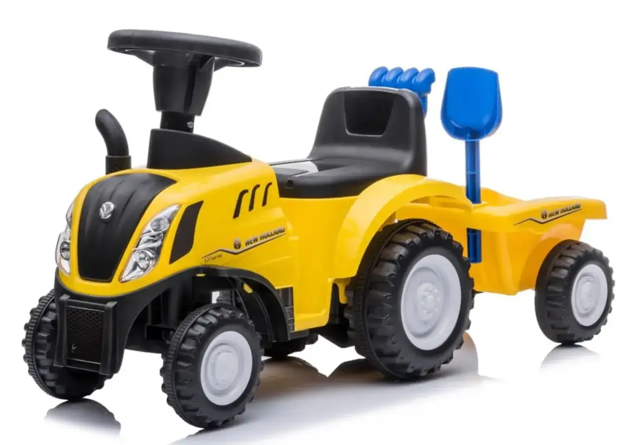Żółty traktor New Holland z przyczepą, zabawka dla małego rolnika. Ma czarne siedzenie, kierownicę i niebieską łopatkę.