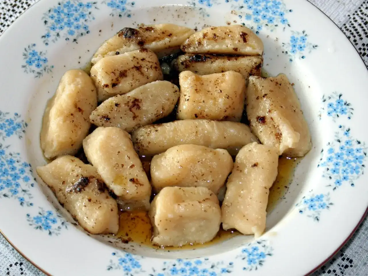 Gotowe pierogi leniwe, polane masłem i posypane cynamonem, czekają na talerzu z niebieskimi kwiatuszkami.