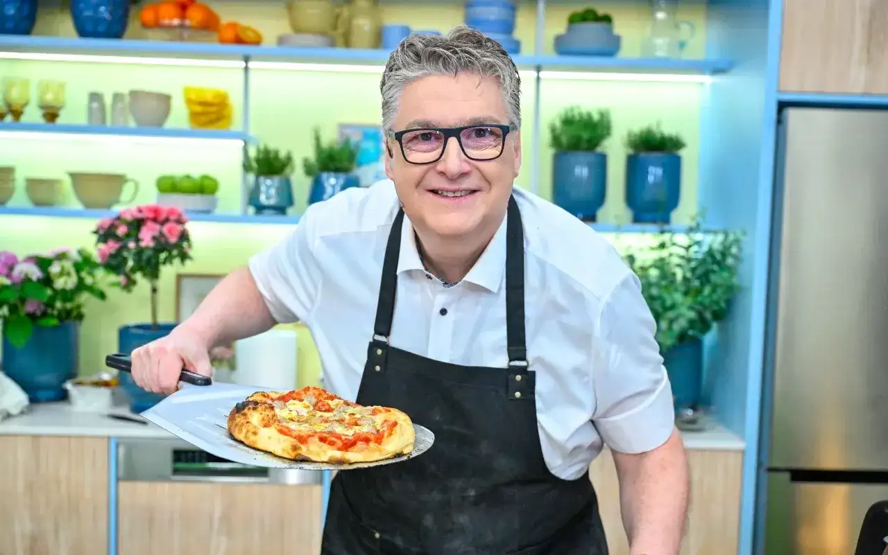 Uśmiechnięty kucharz prezentuje pyszną pizzę rzymską prosto z pieca.