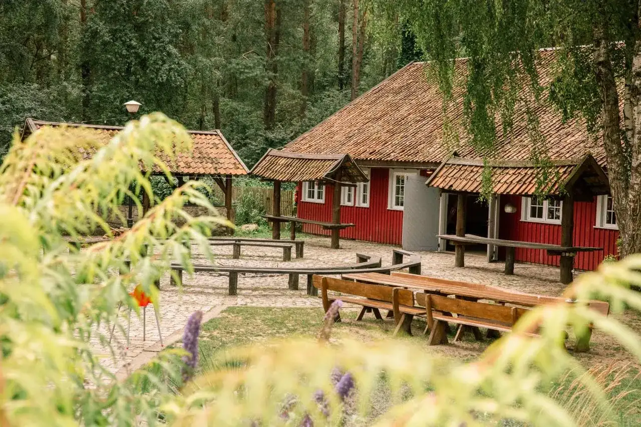 Idealne miejsce na konferencje na Mazurach: czerwony budynek z drewnianymi ławami i stołami w otoczeniu lasu.