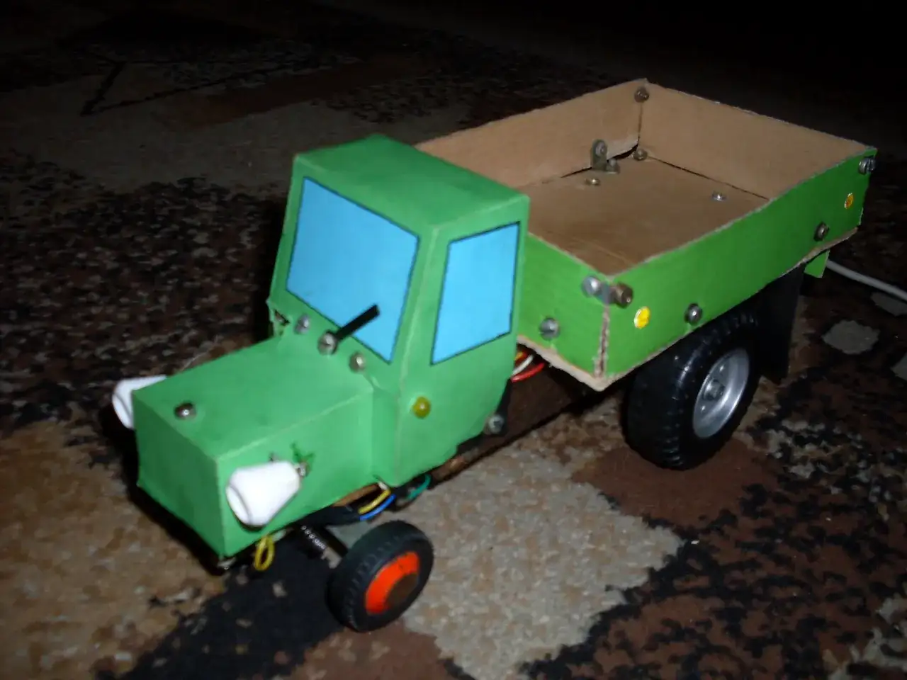Zielony traktor z kartonu, z niebieskimi szybami i drewnianą skrzynią. Oto jak zrobić taki traktor z kartonu!