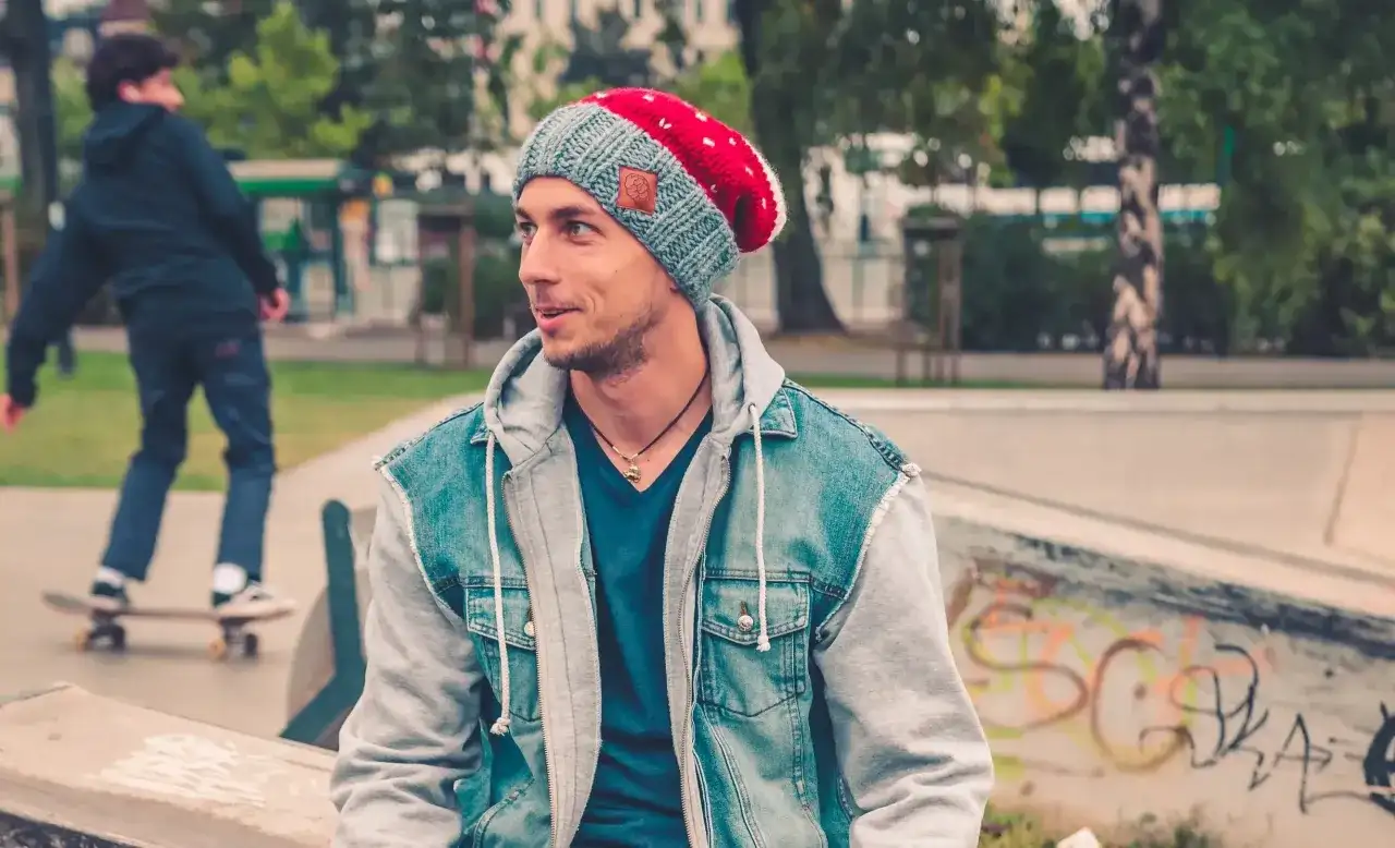 Chłopak w fajnej czapce dla chłopców i jeansowej kurtce siedzi na skateparku.