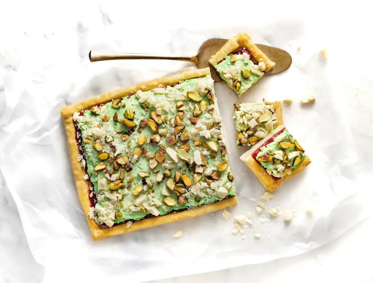 Ciasto z zieloną masą pistacjową i posiekanymi pistacjami, pokrojone na kwadraty.