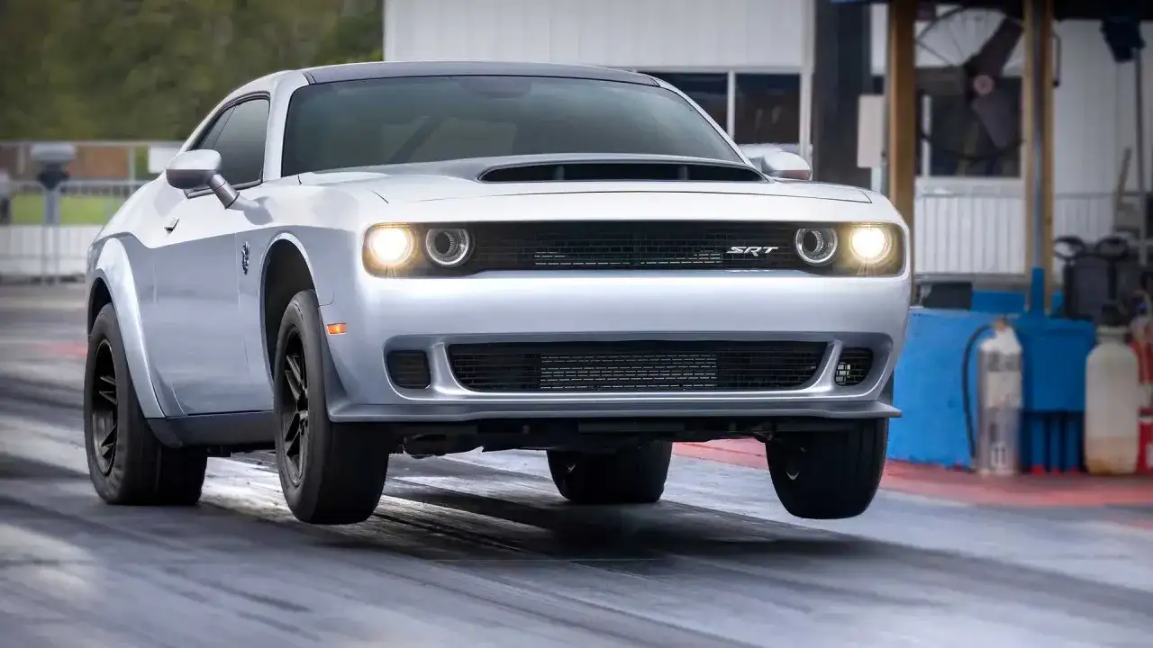 Srebrny Dodge Challenger SRT na torze wyścigowym, z przednimi kołami lekko uniesionymi nad asfaltem.