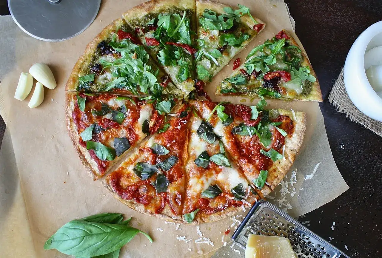 Dwie połówki pizzy: jedna z pesto i rukolą, druga z sosem pomidorowym i bazylią. Zastanawiasz się, ile kosztuje pizza w Czechach?