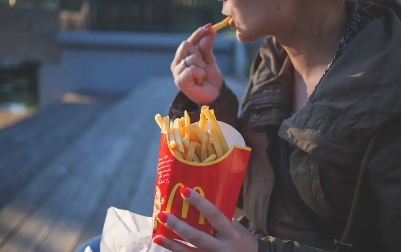 Kobieta je frytki z czerwonego opakowania McDonald's.
