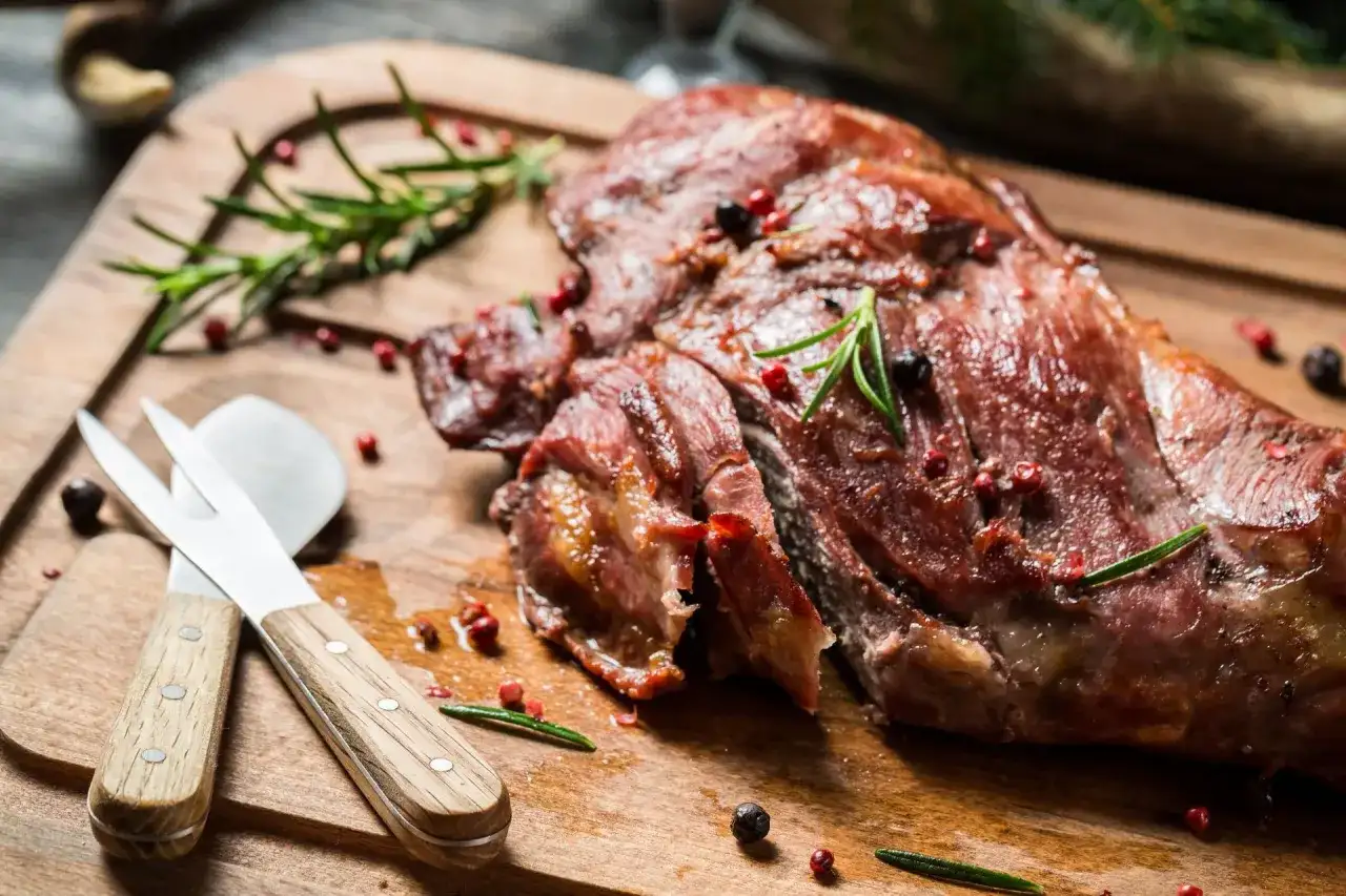 Soczysta dziczyzna, pieczona z rozmarynem i pieprzem, czeka na desce do krojenia. Obok leżą sztućce do mięsa.