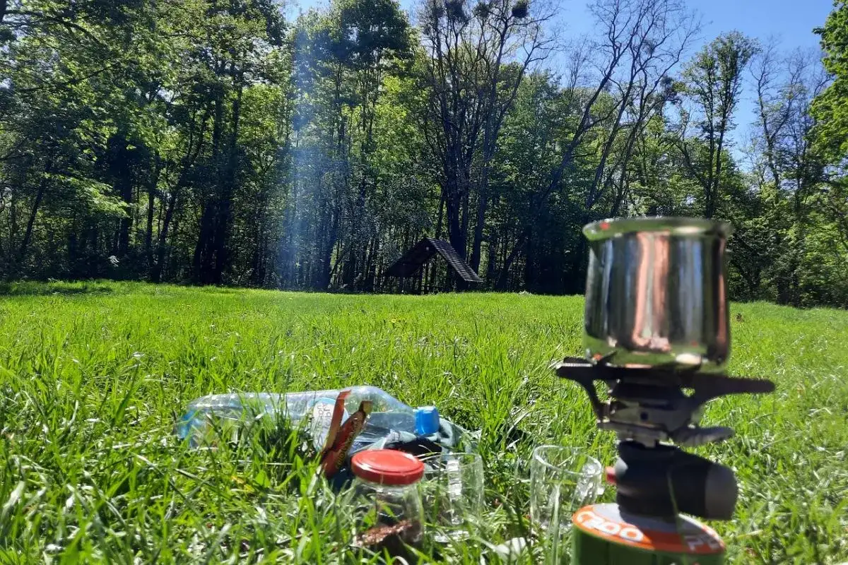 Idealne miejsce, by zanocuj w lesie. Kawa, woda i kuchenka turystyczna na trawie, w otoczeniu drzew.