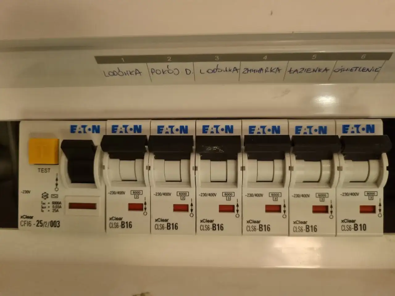 Panel z bezpiecznikami Eaton, z etykietami opisującymi obwody: lodówka, pokój D, zmywarka, łazienka, oświetlenie.
