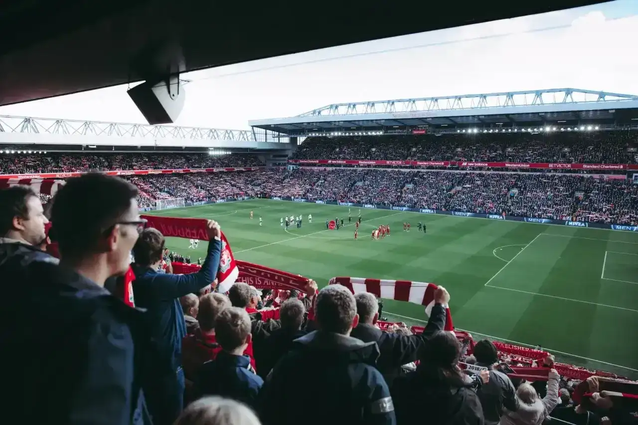 Kibice na stadionie z szalikami, czekają na wznowienie gry. Zastanawiają się, ile trwa przerwa w meczu.