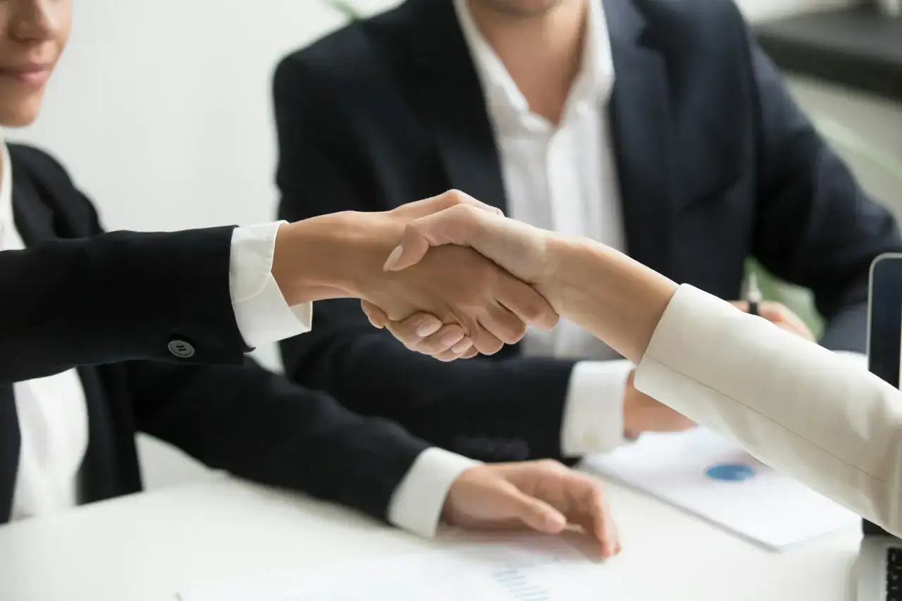Dwie osoby w garniturach ściskają sobie dłonie, symbolizując udaną współpracę. To właśnie jest trade marketing co to znaczy - budowanie relacji biznesowych.