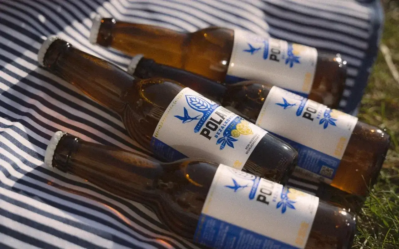 Butelki piwa bezalkoholowego POLAN leżą na kocu. Czy piwo zero ma alkohol? Nie, to piwo jest bezalkoholowe.