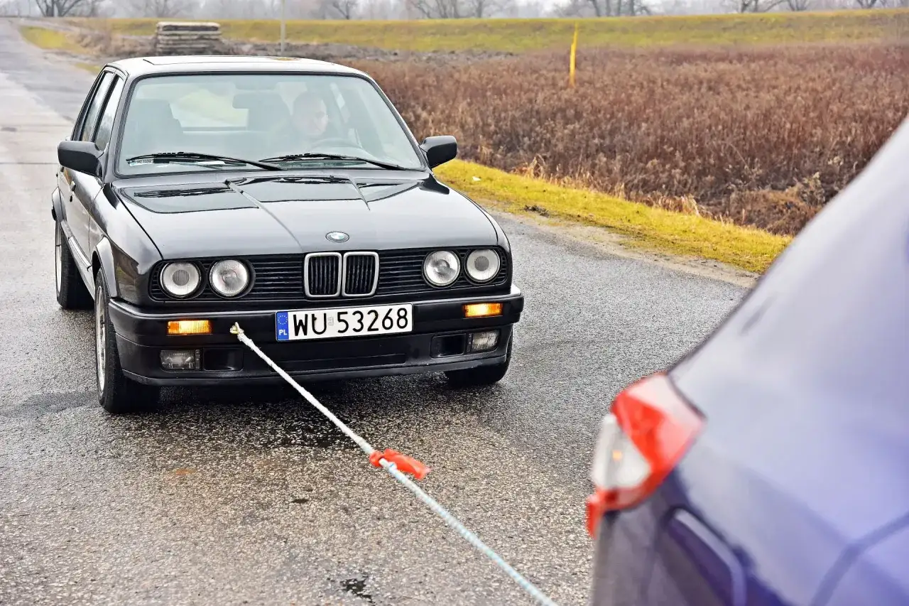 Czarne BMW holowane na mokrej drodze za pomocą liny.