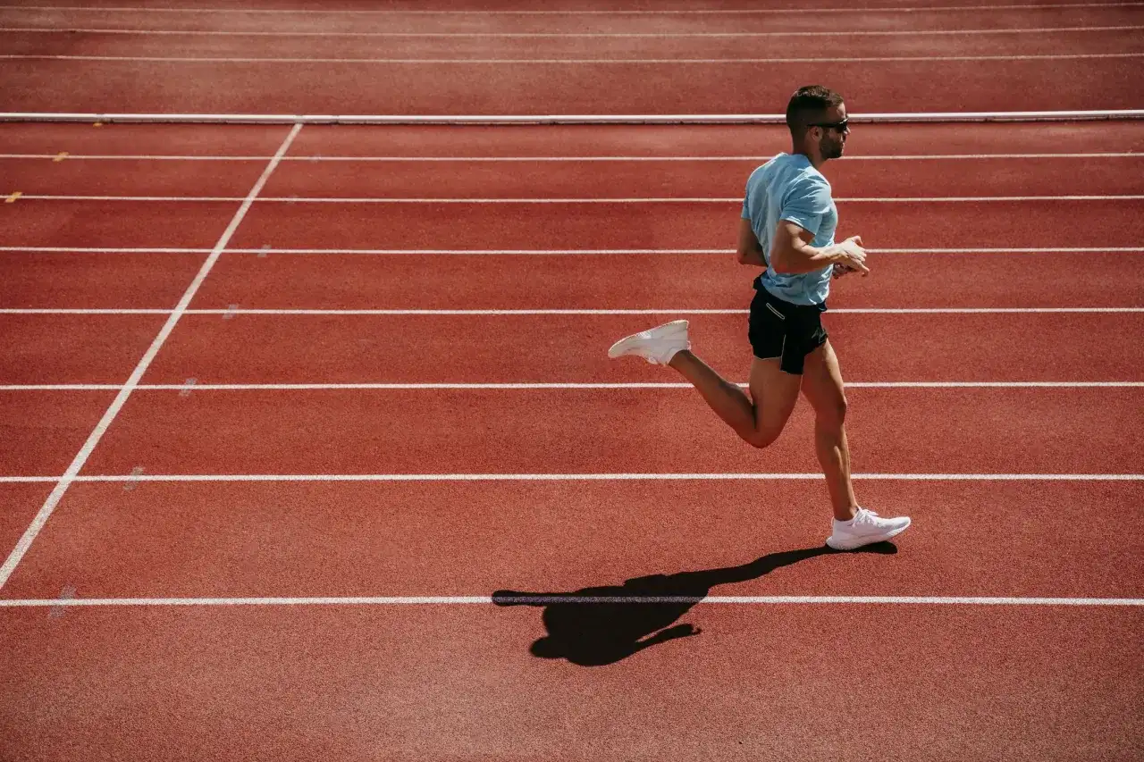 Mężczyzna w niebieskiej koszulce i czarnych spodenkach biegnie po bieżni lekkoatletycznej.