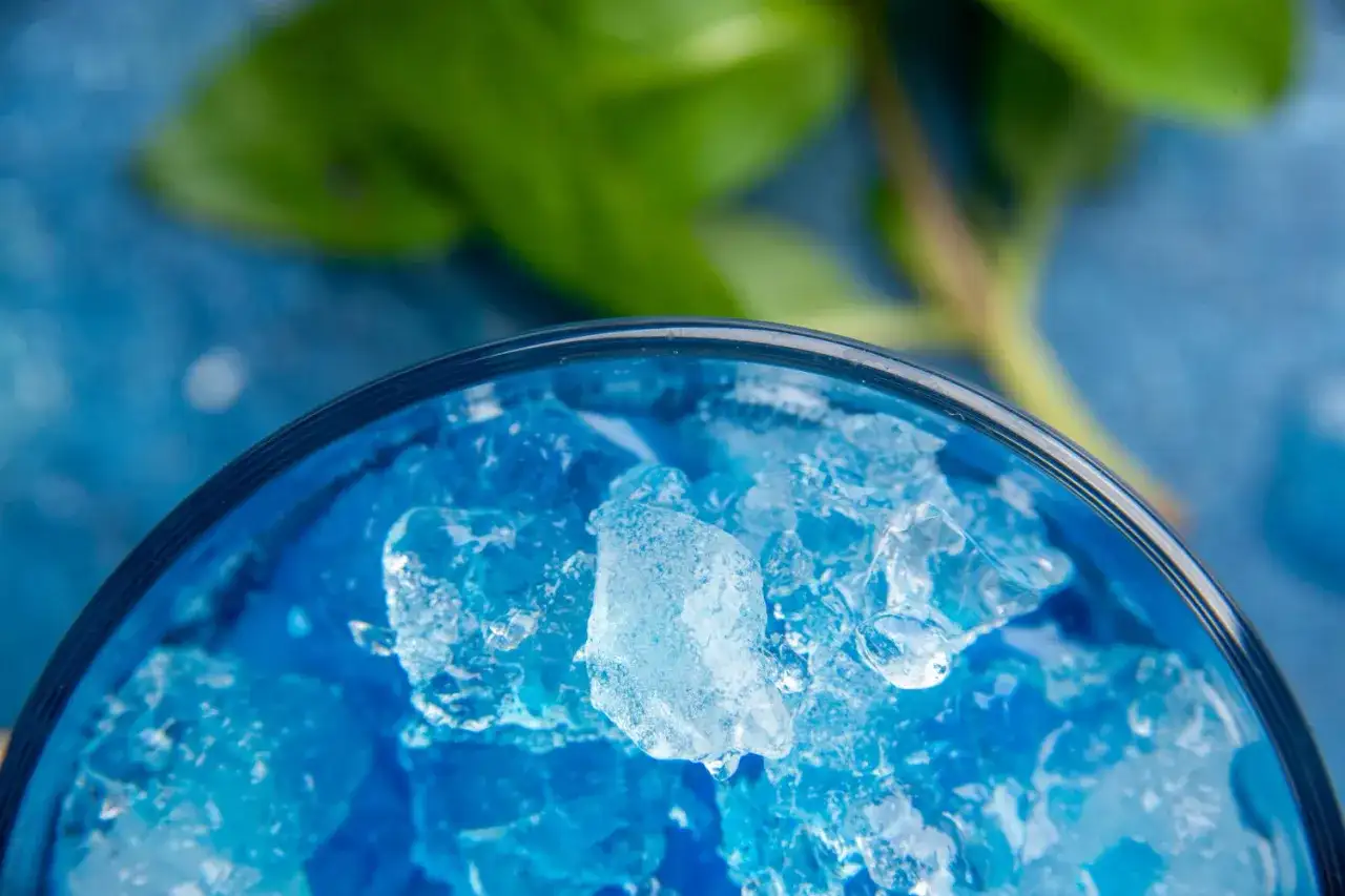 Intensywnie niebieski likier Blue Curacao z kruszonym lodem w szklance, z zielonym liściem w tle.
