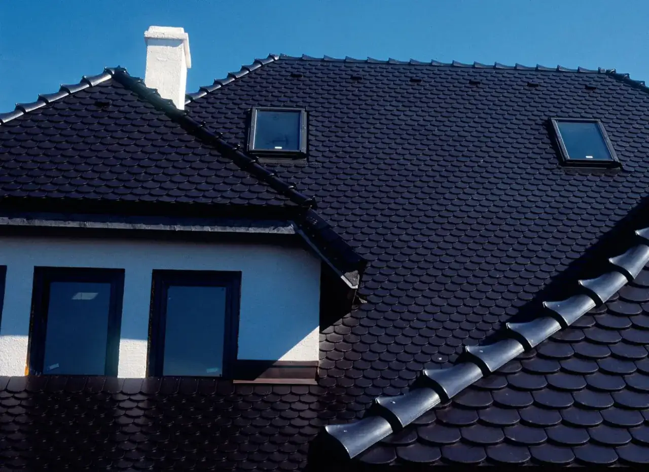 Ciemny dach z dachówki ceramicznej, z kominem i oknami dachowymi. Zastanawiasz się, ile waży paleta dachówki ceramicznej?