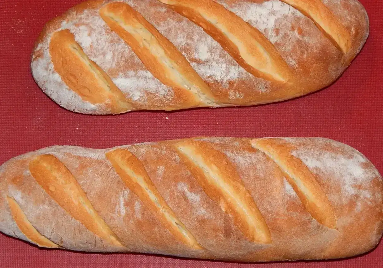 Dwie świeże bułki wrocławskie, lekko oprószone mąką, leżą na czerwonym tle.