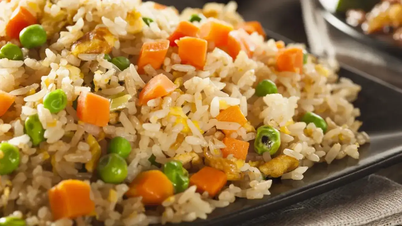 Arroz tres delicias con guisantes verdes, trozos de zanahoria y huevo revuelto, servido en un plato negro.