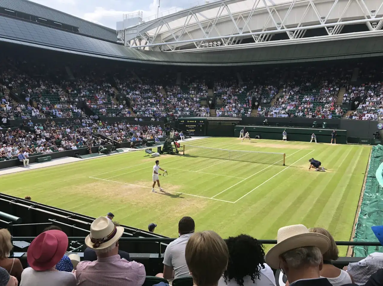 Mecz tenisowy na trawiastym korcie Wimbledonu z widownią na trybunach.