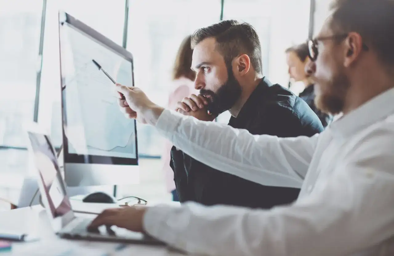 Analityk biznesowy wskazuje na wykres na monitorze, omawiając dane z kolegą.
