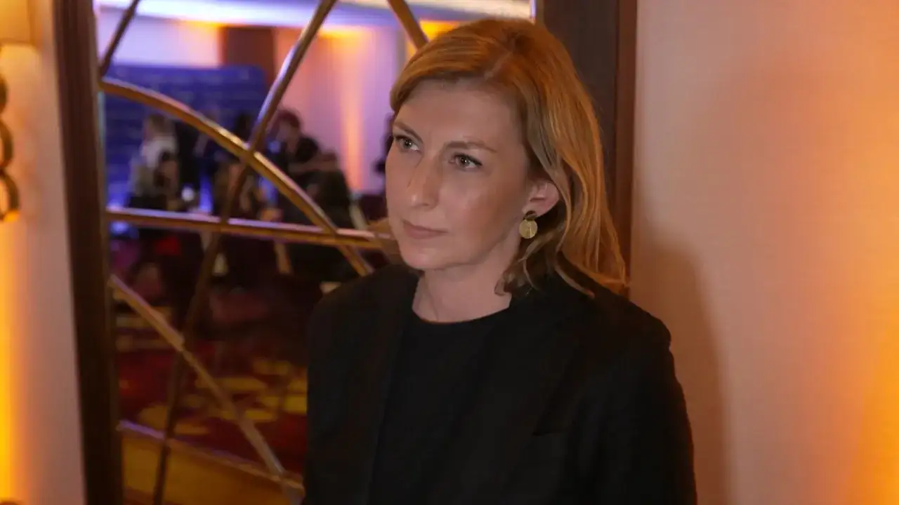 Olga Leonowicz, w wieku około 40 lat, w czarnej marynarce, z blond włosami i złotymi kolczykami, stoi przed lustrem.