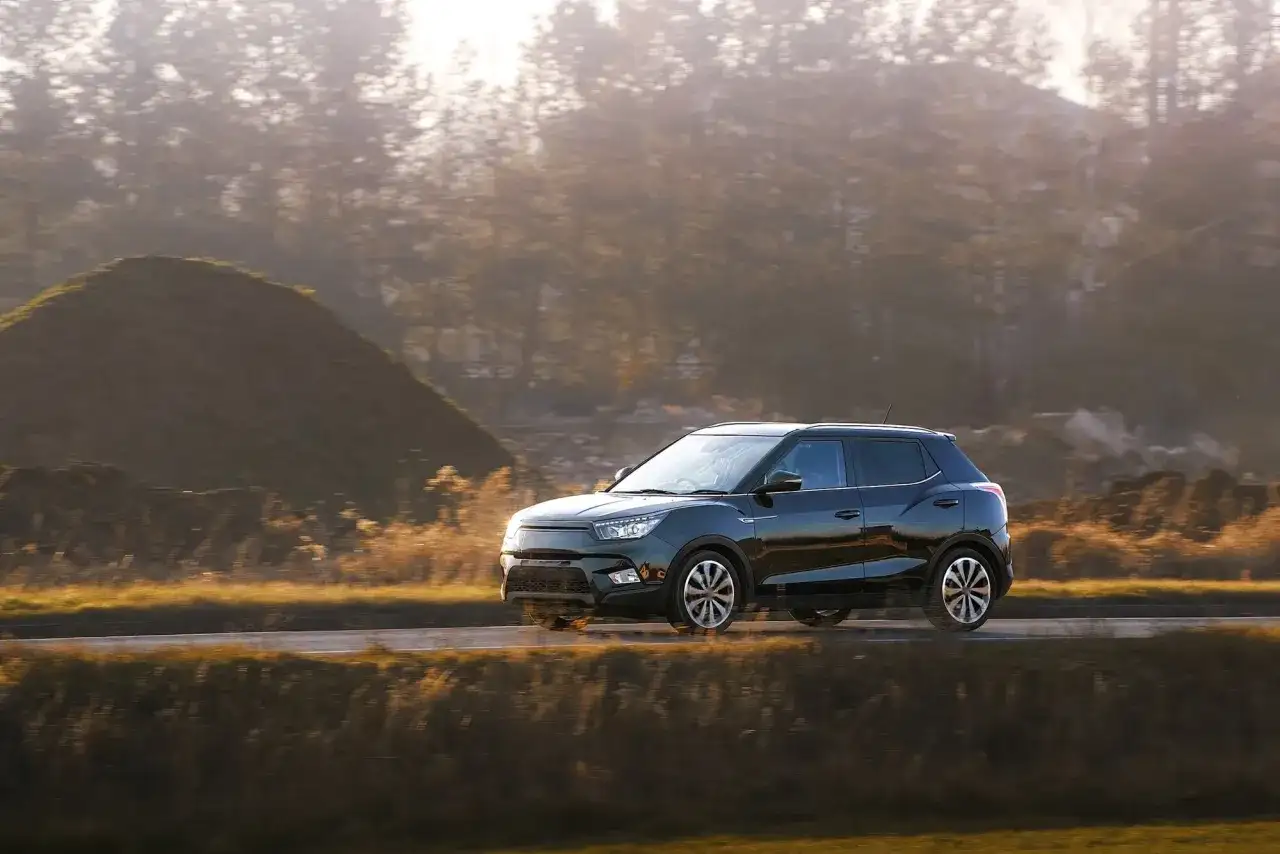 Czarny hatchback jedzie drogą wśród jesiennych wzgórz i drzew.