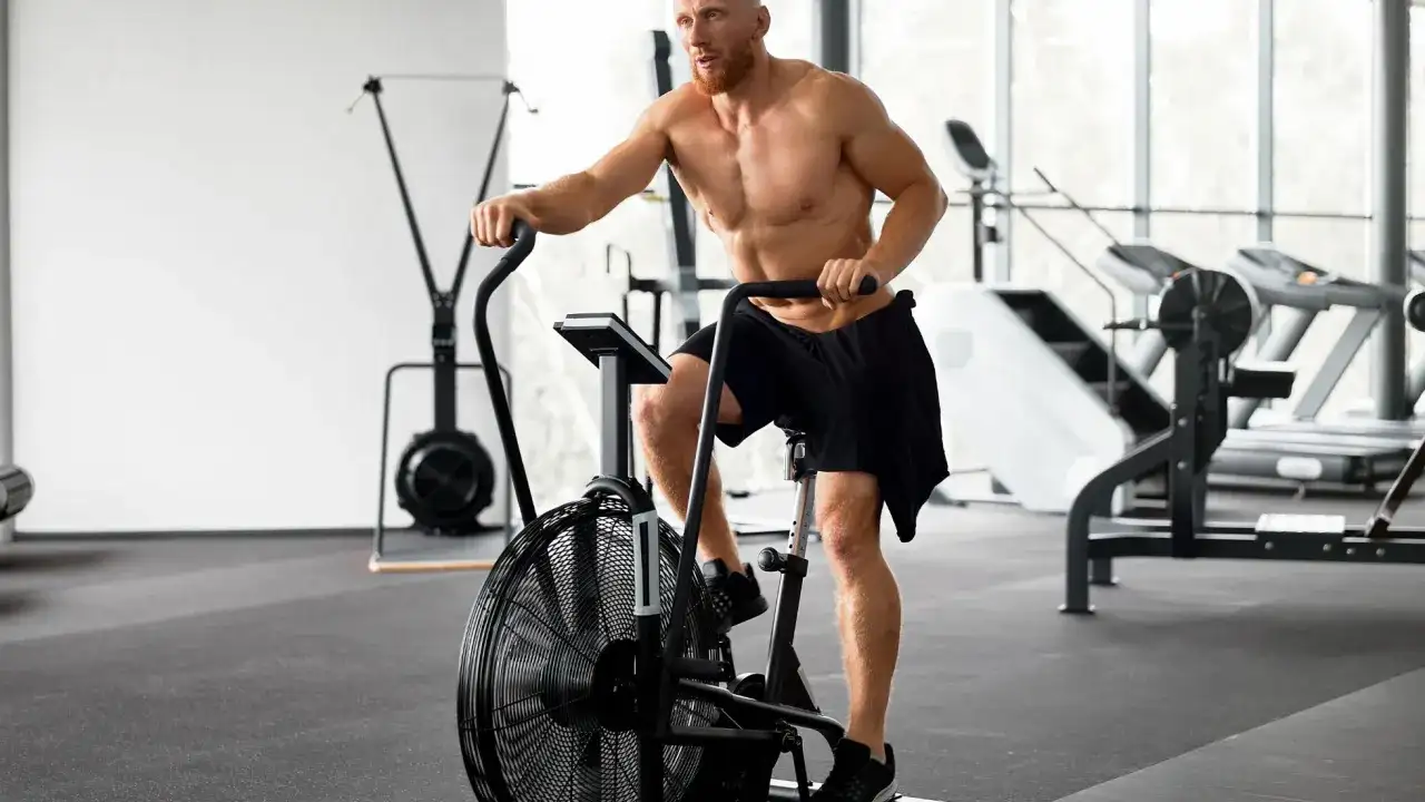 Mężczyzna ćwiczy na rowerze stacjonarnym typu air bike w siłowni.