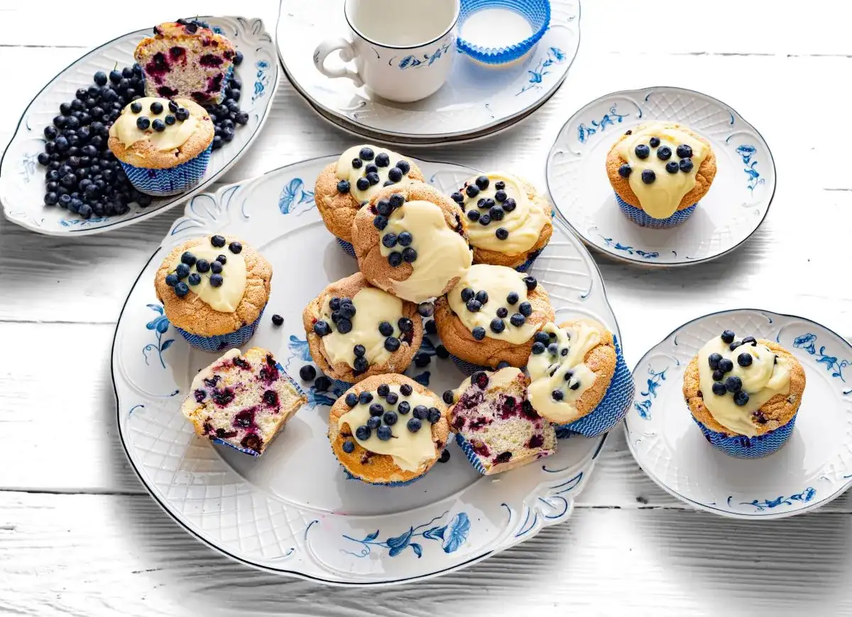 Pyszne muffiny z jagodami, udekorowane kremem i świeżymi owocami, kuszą swoim wyglądem i zapachem.
