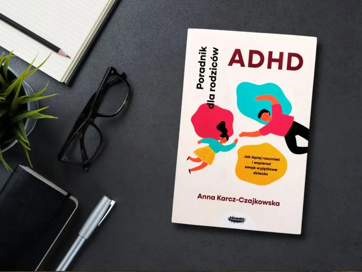 Książka "ADHD. Poradnik dla rodziców" Anny Karcz-Czajkowskiej, z ilustracją rodzica i dziecka. Obok notatnik, okulary i długopis.