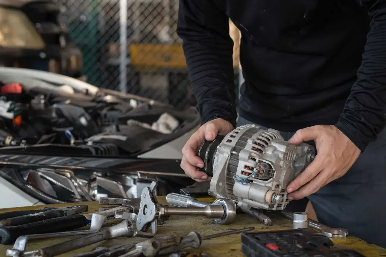 Mechanik trzyma alternator, zastanawiając się, ile trwa regeneracja alternatora. Na stole leżą narzędzia.