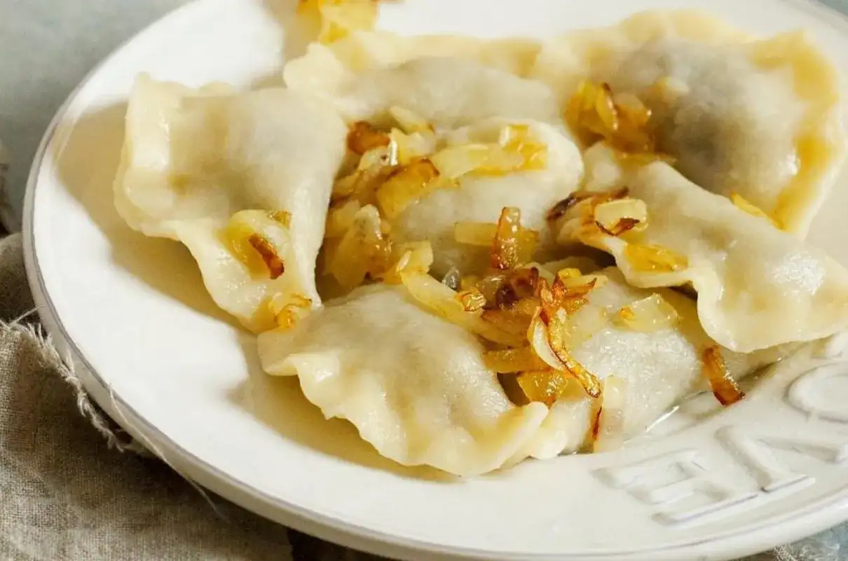 Pyszne pierogi ruskie na talerzu, polane skwarkami z cebulki. Idealne, gdy wiesz, jak długo gotować pierogi ruskie.