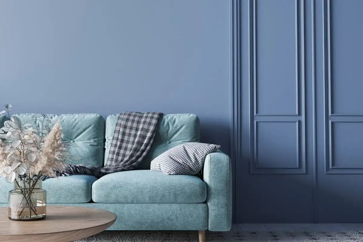 Miętowa kanapa z kocem i poduszką na tle ścian w kolorze baby blue. To znaczy spokój i świeżość.