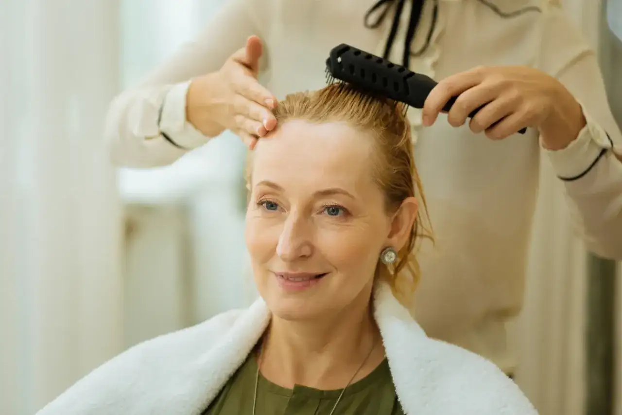 Stylist czesze blondynce cienkie i rzadkie włosy, przygotowując ją do nowej fryzury.