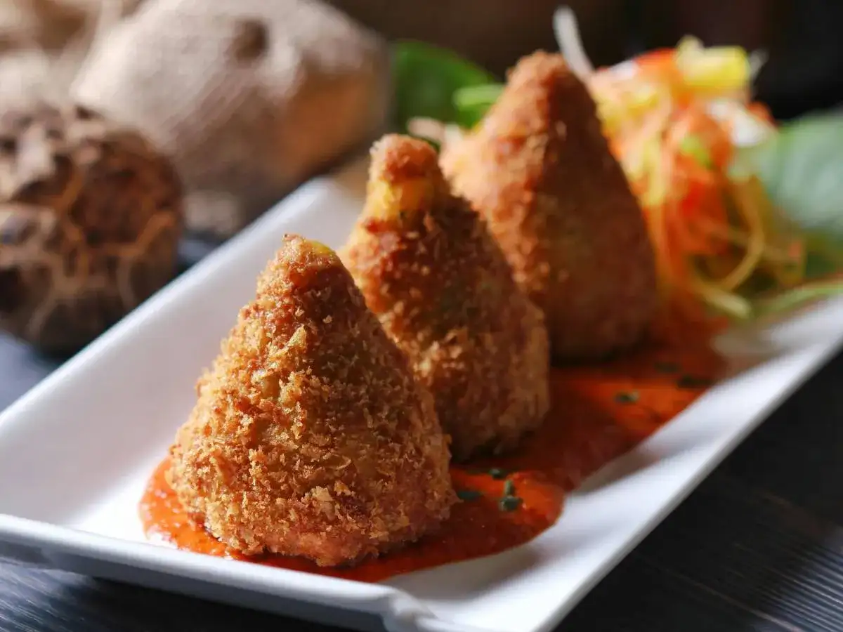 Trzy złociste arancini, smażone kulki ryżowe, podane na sosie pomidorowym z sałatką. Pyszne arancini co to?
