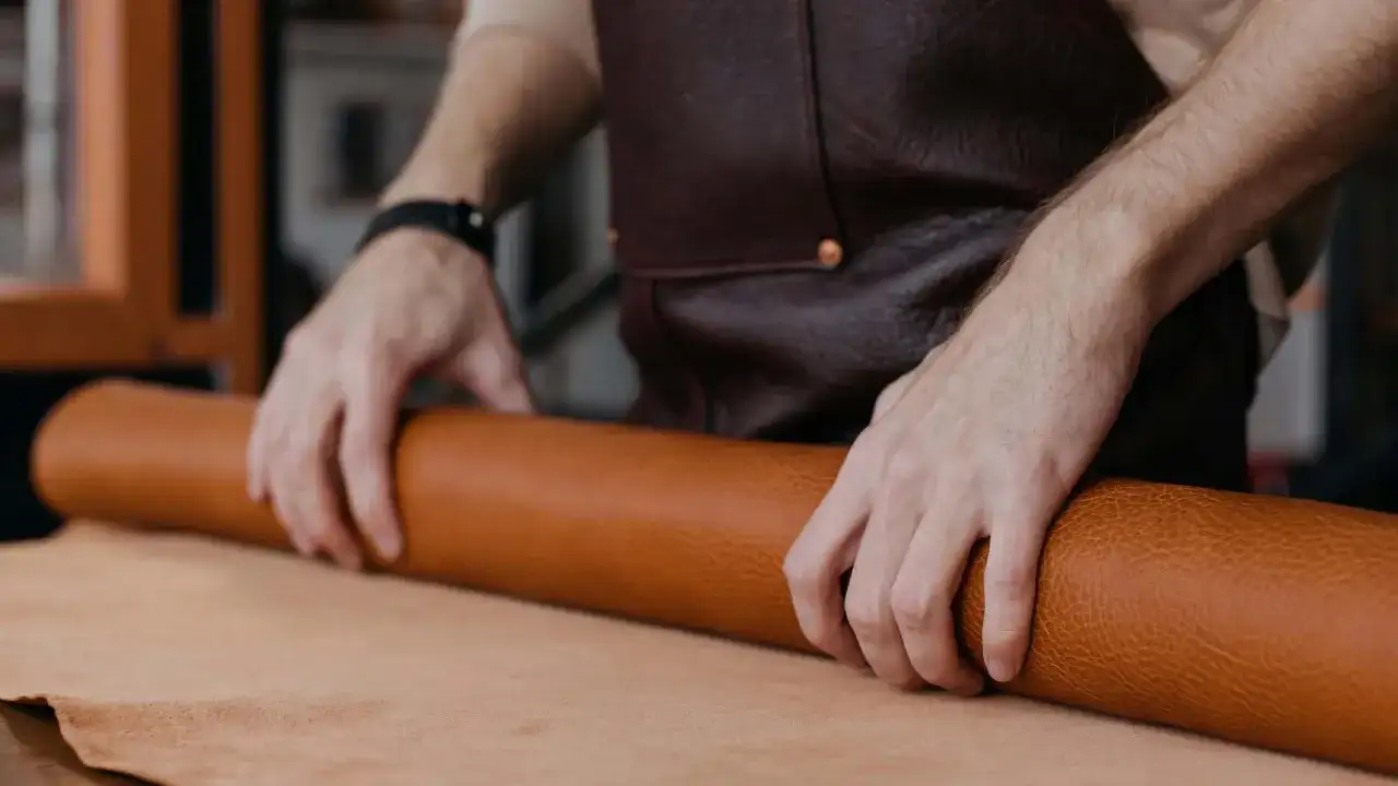 Manos de artesano desenrollando un rollo de cuero, mostrando la textura y el color natural del material. Se pregunta de que esta hecho el cuero.