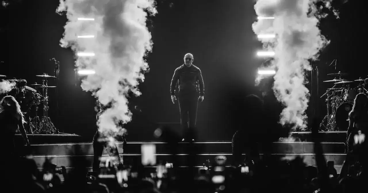 Pitbull na scenie, otoczony dymem i światłami, podczas koncertu.
