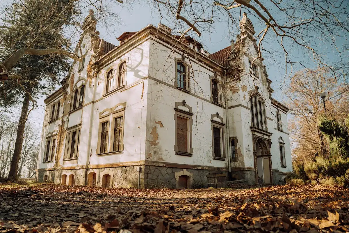 Opuszczony pałac w Polsce, zniszczony tynk i suche gałęzie drzew tworzą melancholijny obraz.