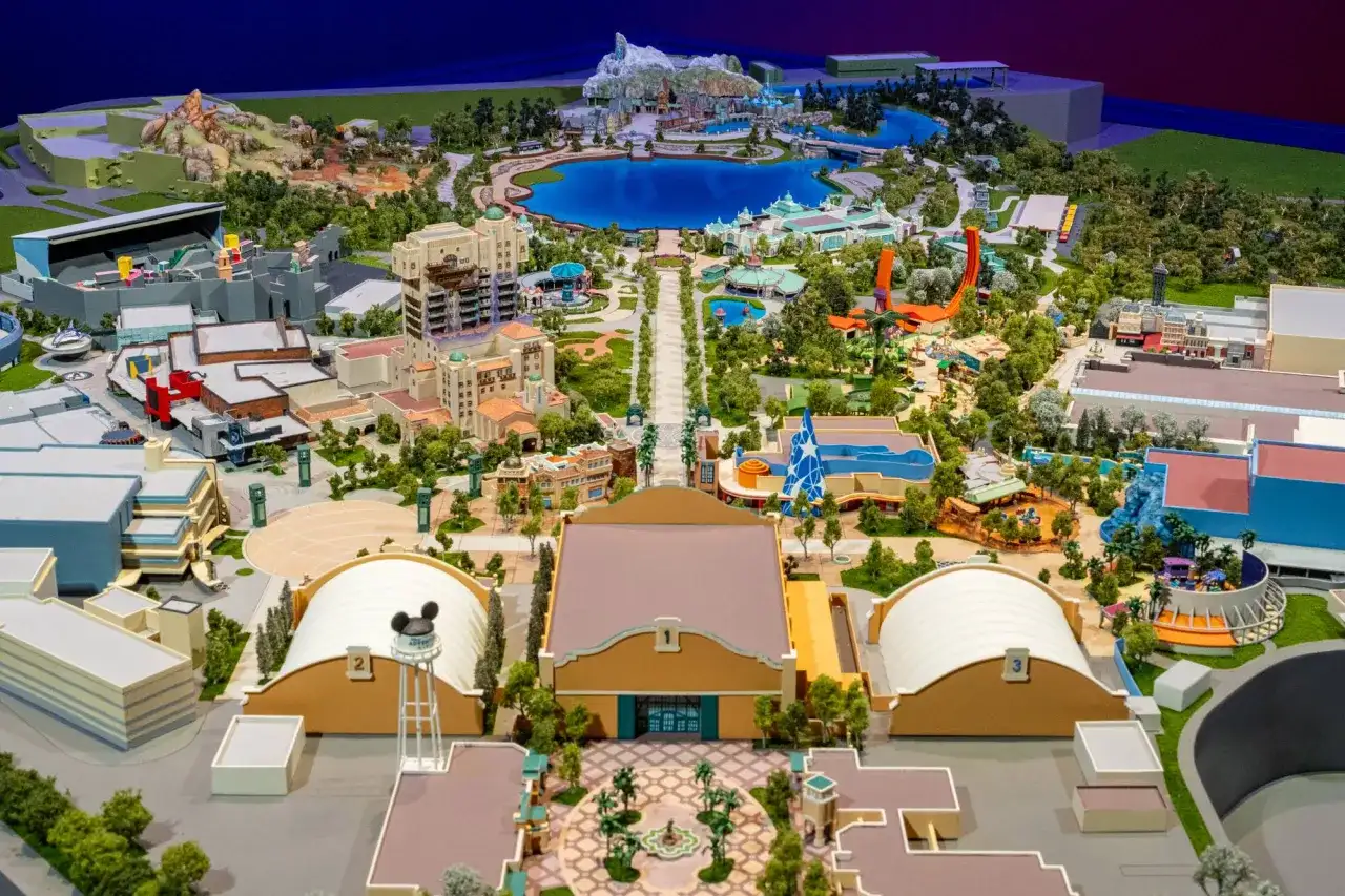 Maquette détaillée d'un parc d'attractions Disney avec lac, montagnes, bâtiments et attractions.