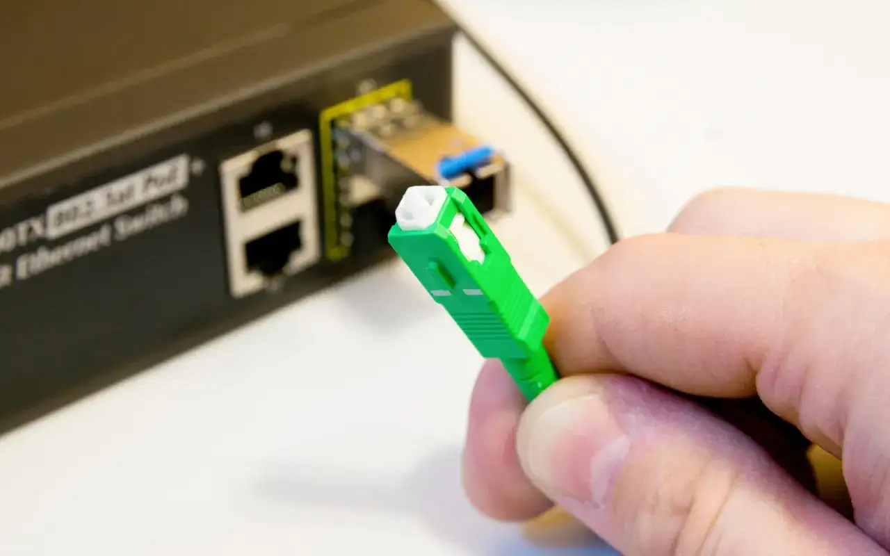 Zielona wtyczka światłowodu gotowa do podłączenia do switcha w bloku. Szybki internet w zasięgu ręki.